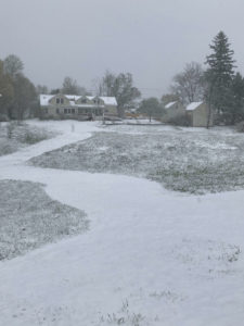 Snowy day with house and barn in the distance beyond a wide white path.