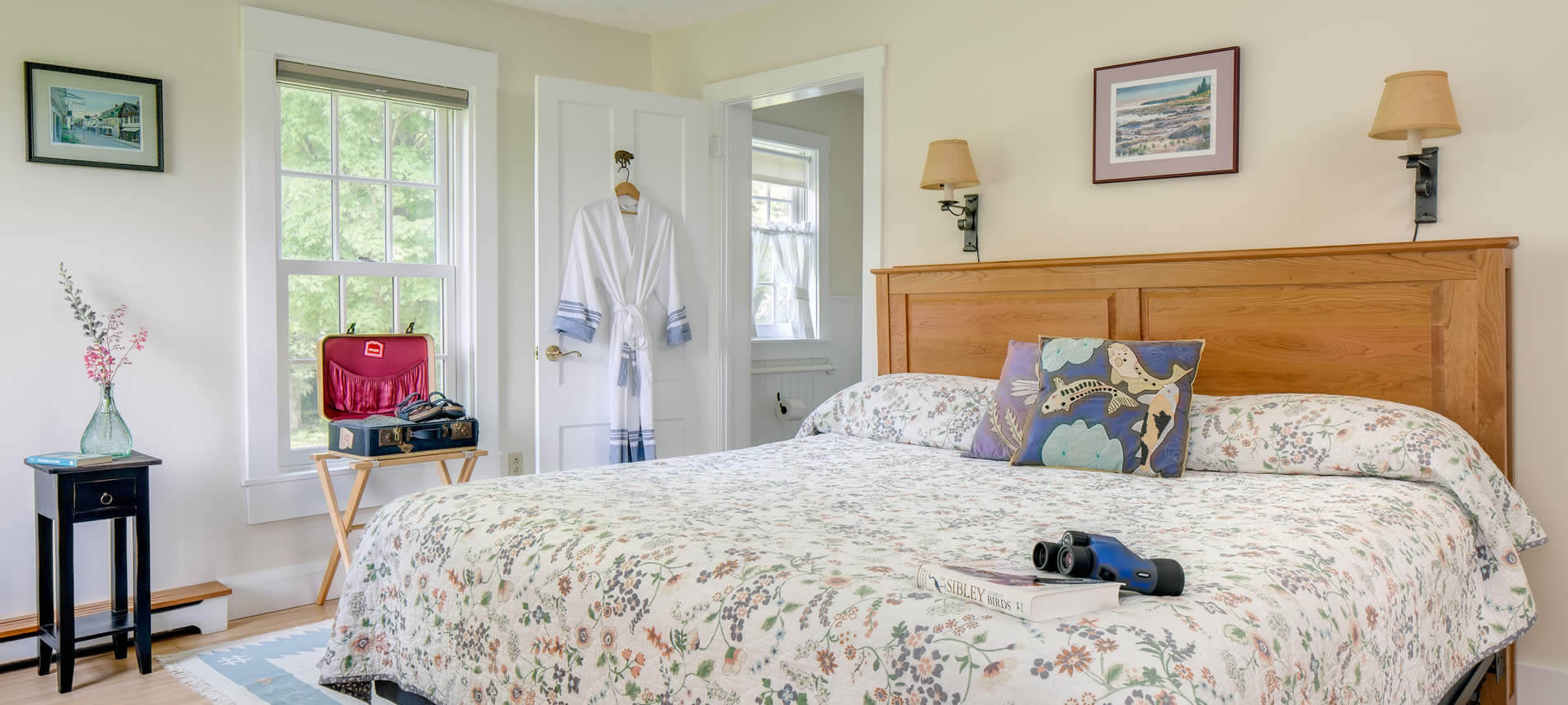 Bright beige room with trim and doors, wood floor, and two sconce lights over a wood bed with floral bedspread
