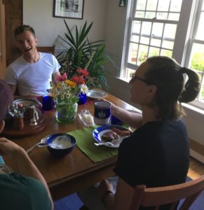 A young man in a white-shirt shirt and woman sitting across from each other at a colorful breakfast table laugh at something another guests said.