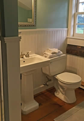 Bathroom with light blue walls, white beadboard, white stool and pedestal sink and wide plank wood floors